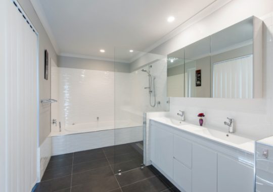 A large renovated bathroom design with a glass shower wall and mirrors on the medicine cabinet above the vanity