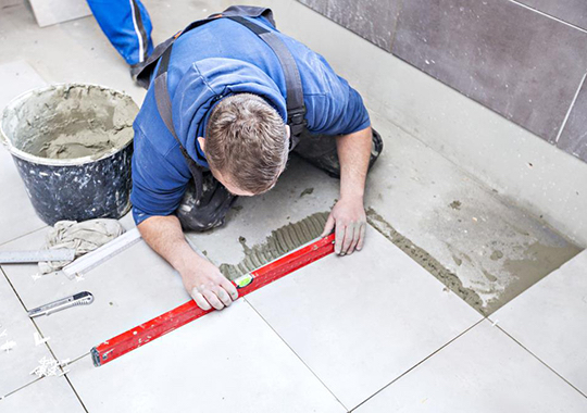 A WA Assett employee lays new tiles during a bathroom renovation