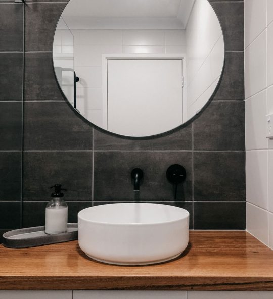 round mirror with modern sink below and black taps