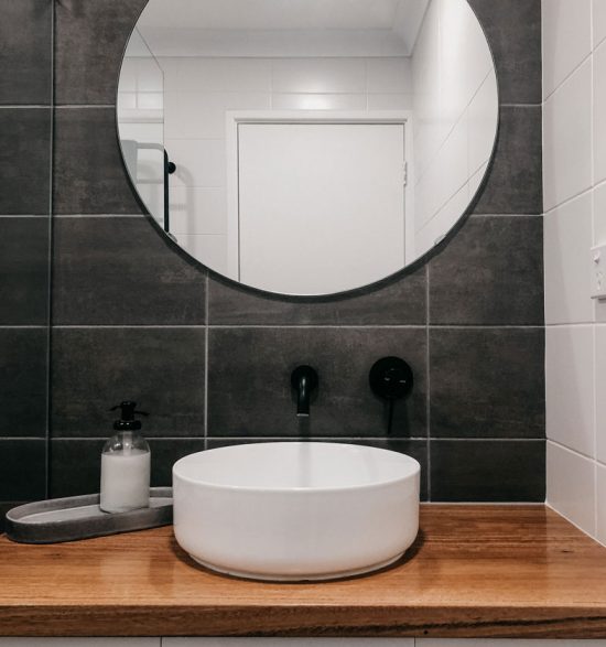 round mirror with modern sink below and black taps