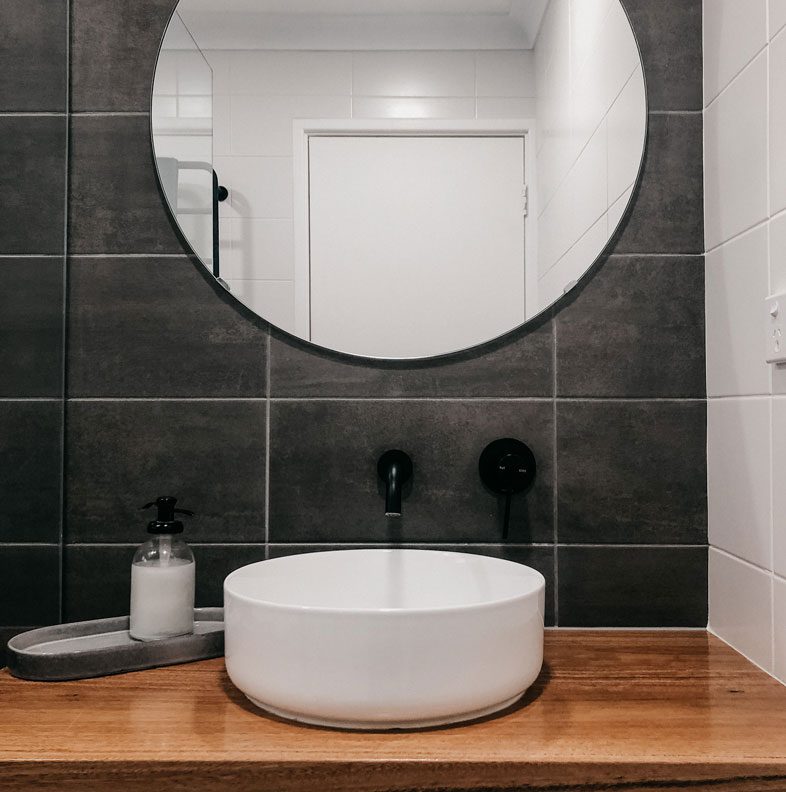 round mirror with modern sink below and black taps