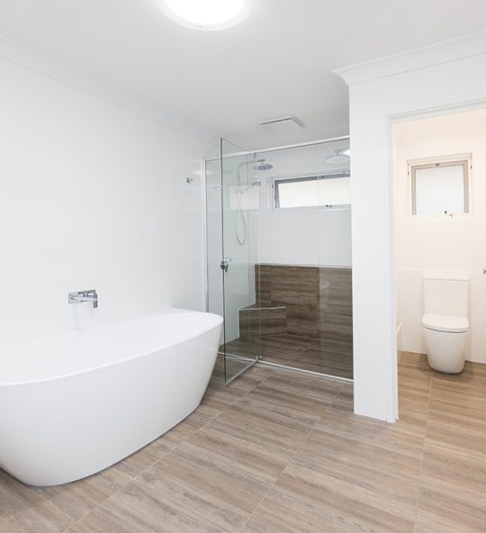 This renovated bathroom features a rounded freestanding bathtub, back-to-wall toilet, and large shower with a glass pane door
