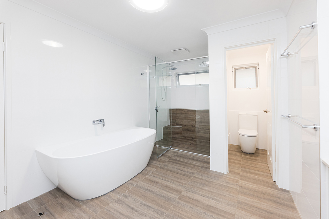 This renovated bathroom features a rounded freestanding bathtub, back-to-wall toilet, and large shower with a glass pane door