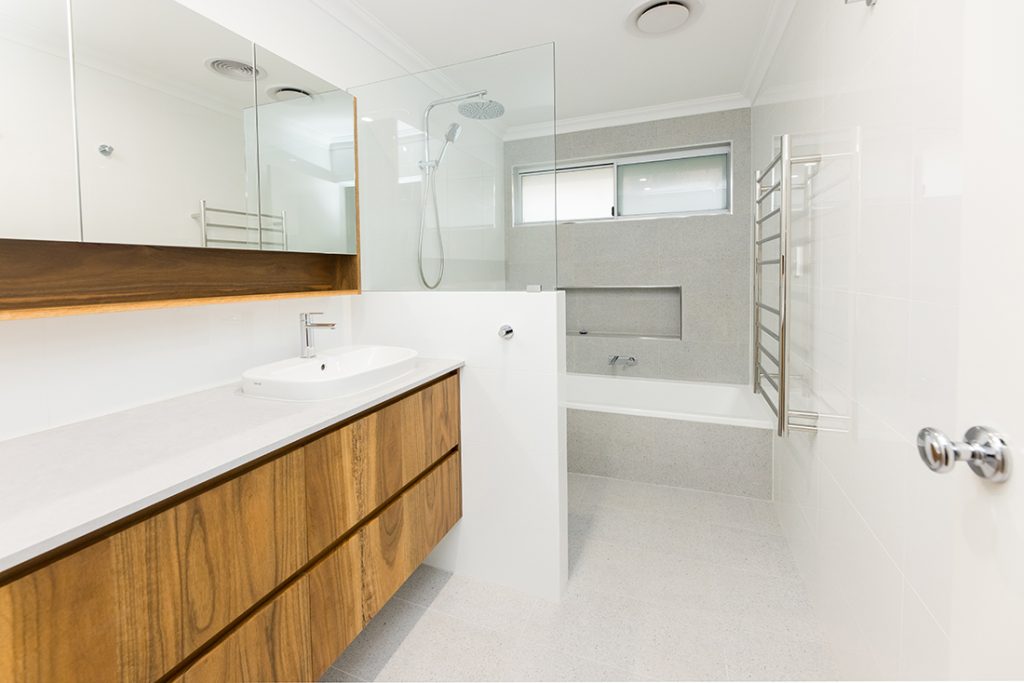 This bathroom features a large countertop and overhead storage cupboard space around the vanity, a nib wall to separate the vanity from the walk-in shower, and a low inbuilt bathtub