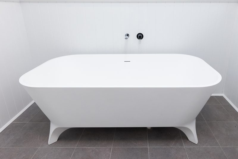 A large, white freestanding tub is installed in this new bathroom design with chrome tapware