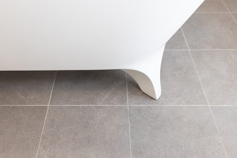 A freestanding bathtub is installed over light grey tiling