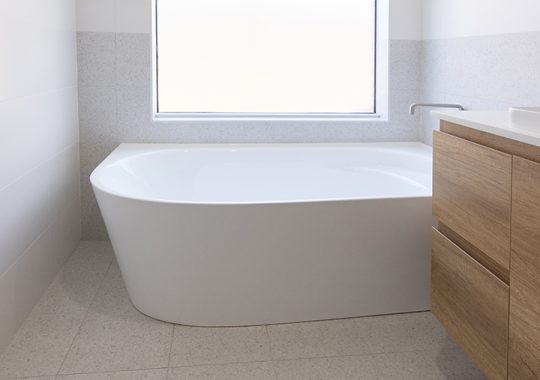 A freestanding tub is installed by a window which lets in plenty of natural light into the bathroom