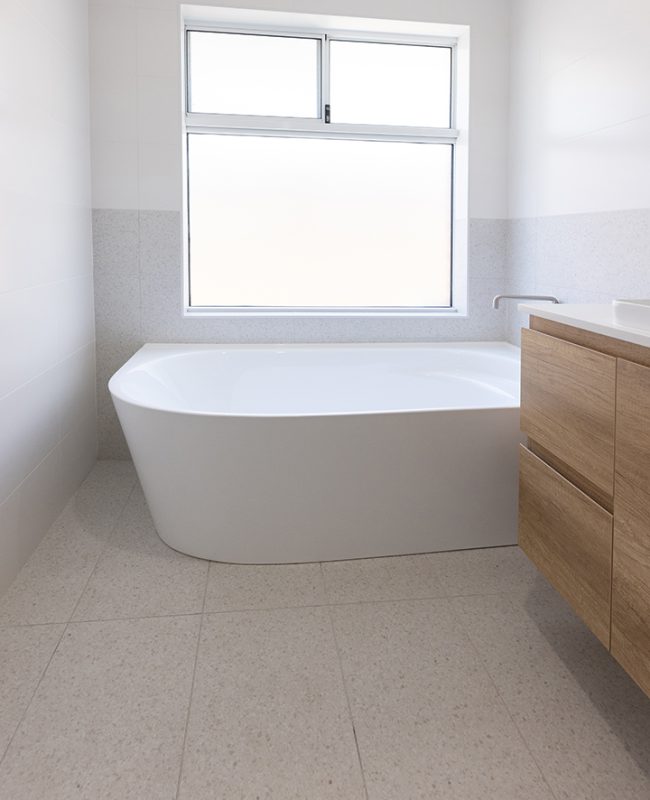 A freestanding tub is installed by a window which lets in plenty of natural light into the bathroom