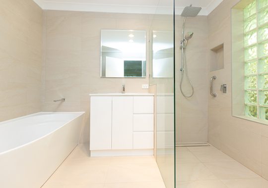 A bright, newly-renovated bathroom with cream tiles and a walk-in shower