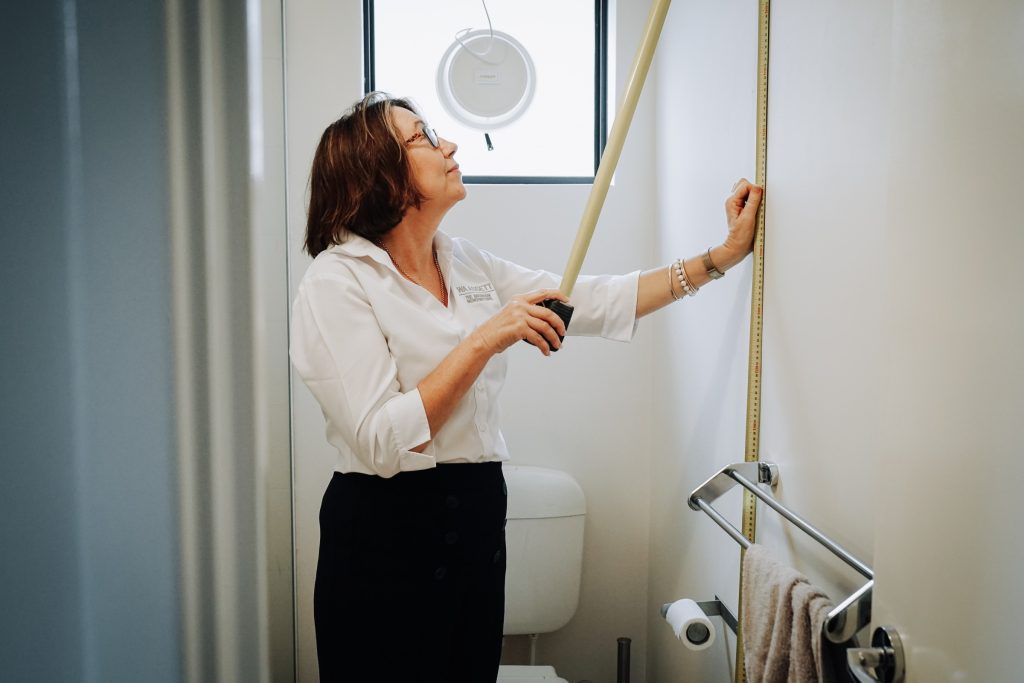 A bathroom renovation consultant measures the wall height in a bathroom.