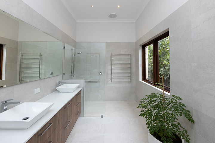 A modern bathroom design with a walk-in shower, light grey tiling, a double vanity, and large pot plant