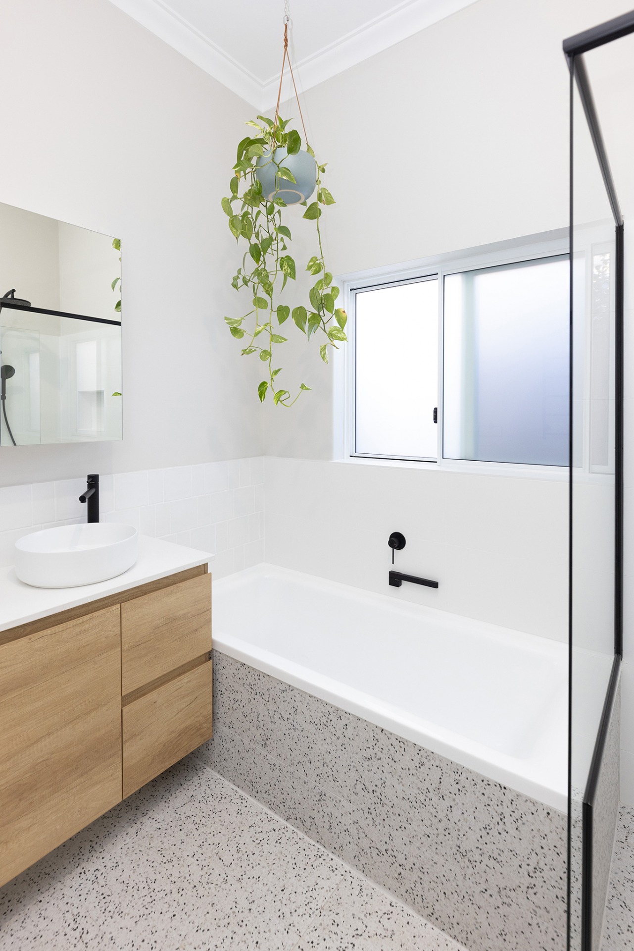 A bathroom with a plant hanging above a renovated bath