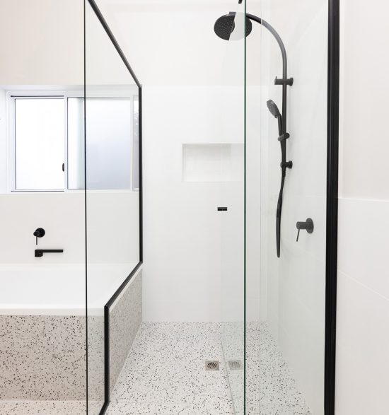 A spacious shower with a black frame, white wall tiles and bathtub.