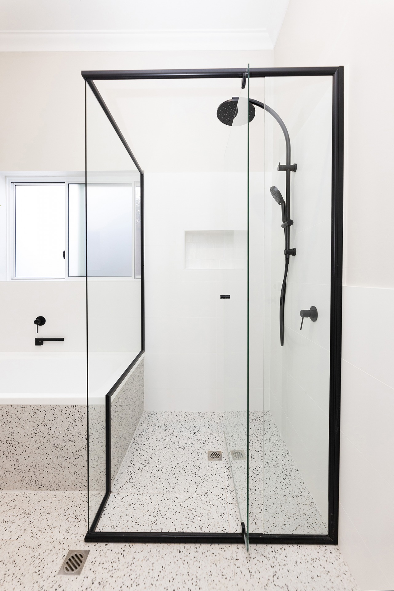 A spacious shower with a black frame, white wall tiles and bathtub.
