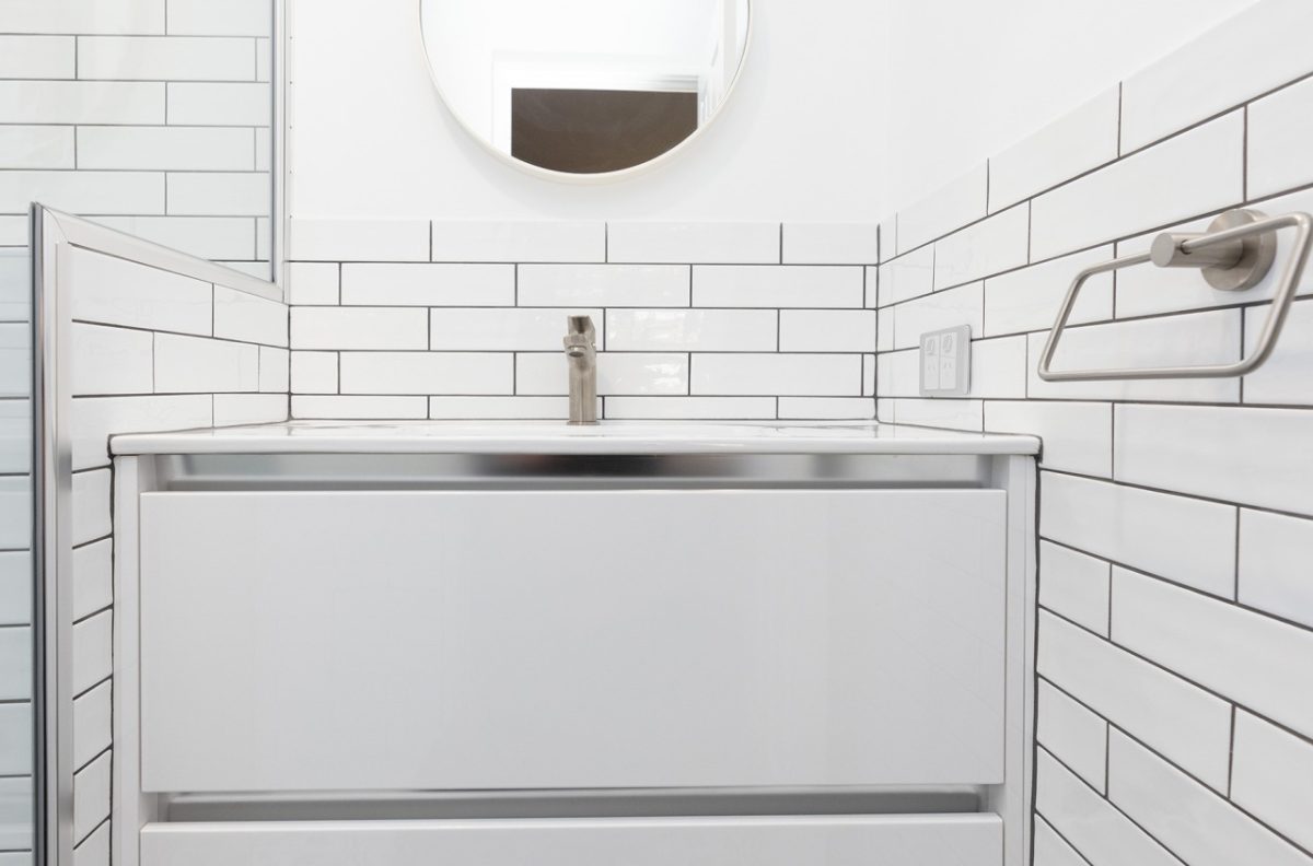 White vanity with a small circular mirror above and white tiles