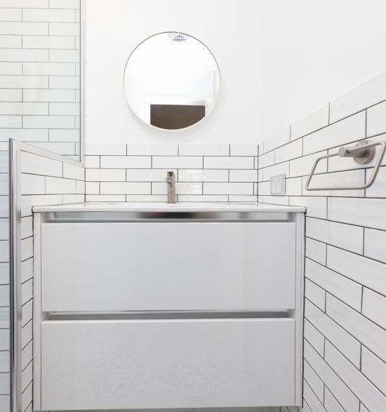 White vanity with a small circular mirror above and white tiles