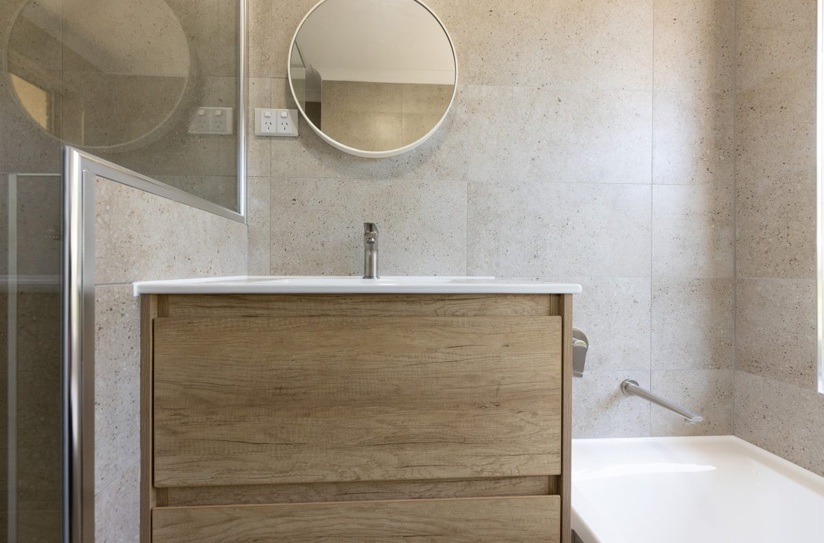 Vanity with wood tones, framed by cream coloured tiles