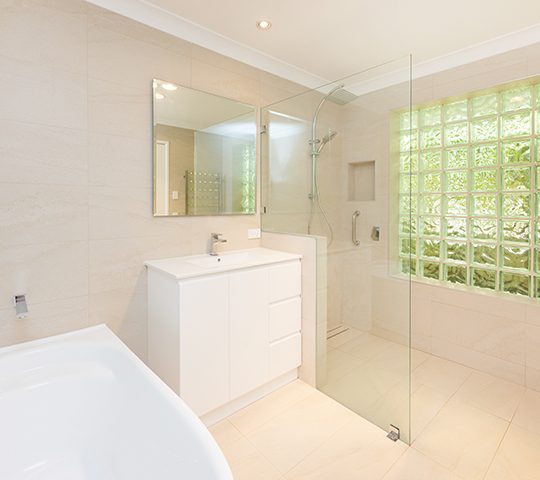 Cream and white bathroom with a large bath, which has accessible railings for support