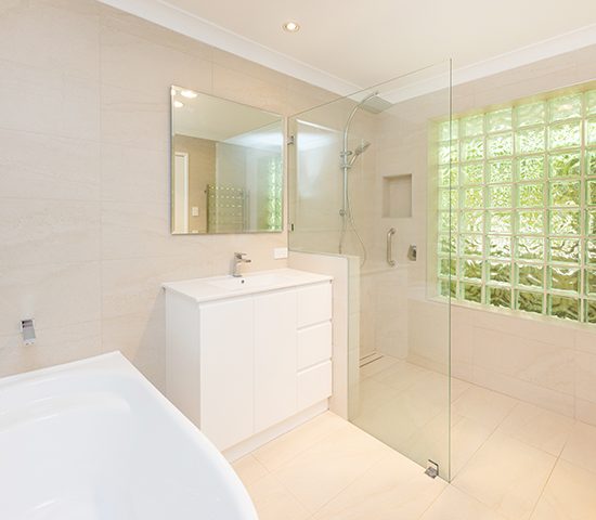 Cream and white bathroom with a large bath, which has accessible railings for support