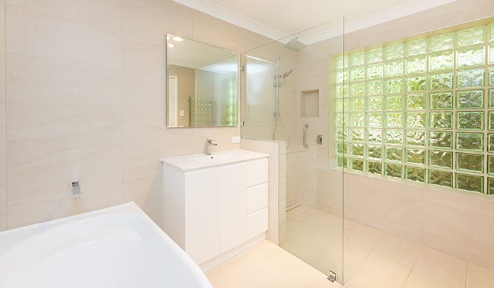 Cream and white bathroom with a large bath, which has accessible railings for support