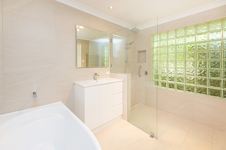 Cream and white bathroom with a large bath, which has accessible railings for support