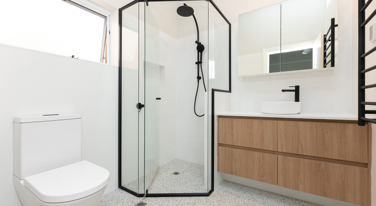 Spacious shower lined with black, beside a large vanity